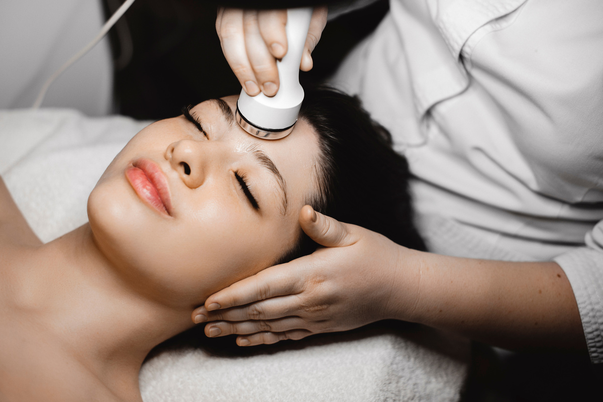 Close up of a charming young woman having electroporation procedure while leaning on a spa bed with eyes closed in a wellness spa center.